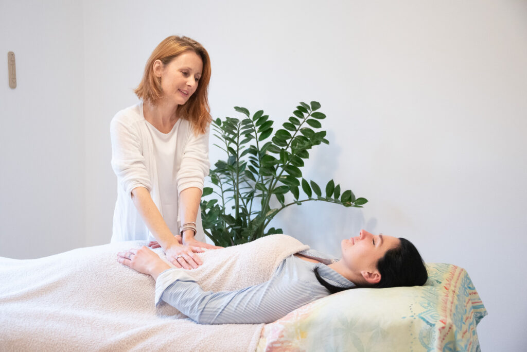 Reiki terapija, ki jo izvaja Ana Bergant na ženski, ki leži na masažni mizi.